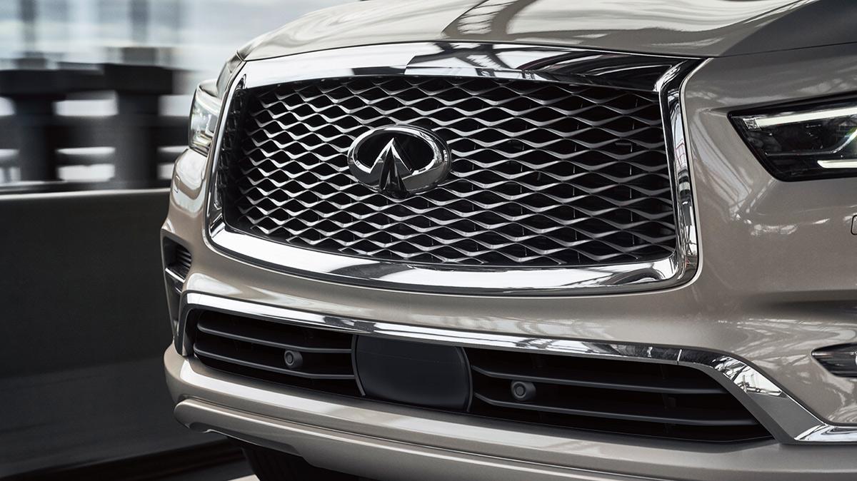 Close-up view of a tan INFINITI QX80 grille on a city street. Close-up view of a tan INFINITI QX80 grille on a city street.