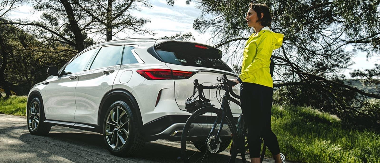 A woman loading a bike into her INFINITI QX50 on a country road. A woman loading a bike into her INFINITI QX50 on a country road.