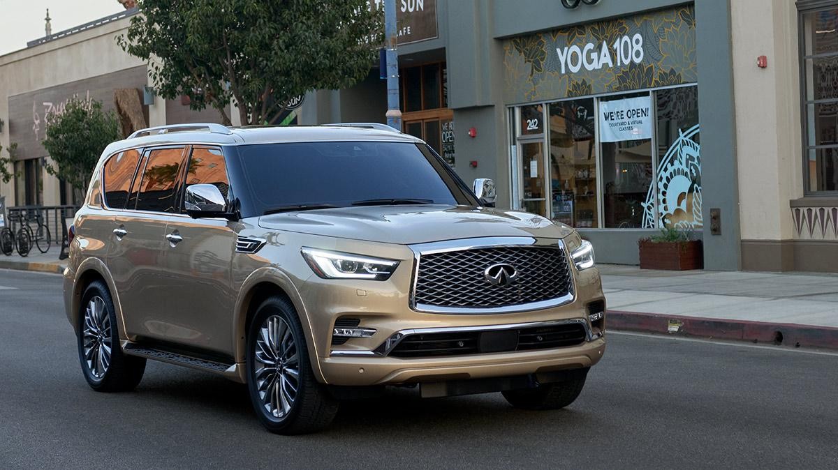 A tan INFINITI QX80 driving down a city street at sunset.