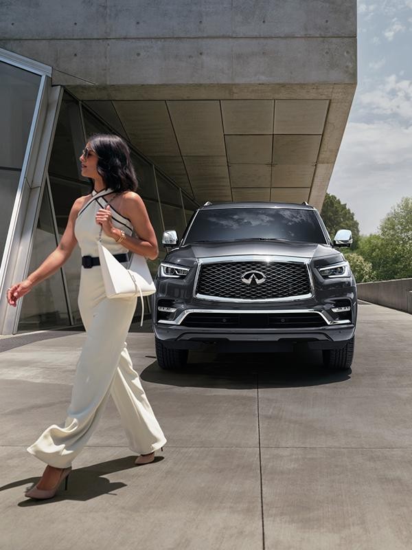 Head-on view of a grey INFINITI QX80 with a woman walking by.