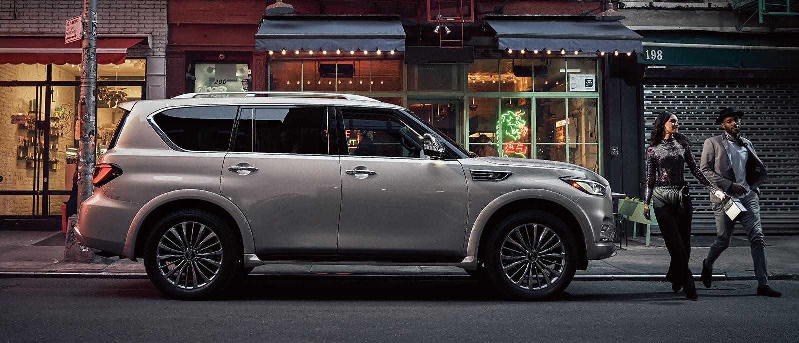 A silver INFINITI QX80 parked on a city street at dusk.