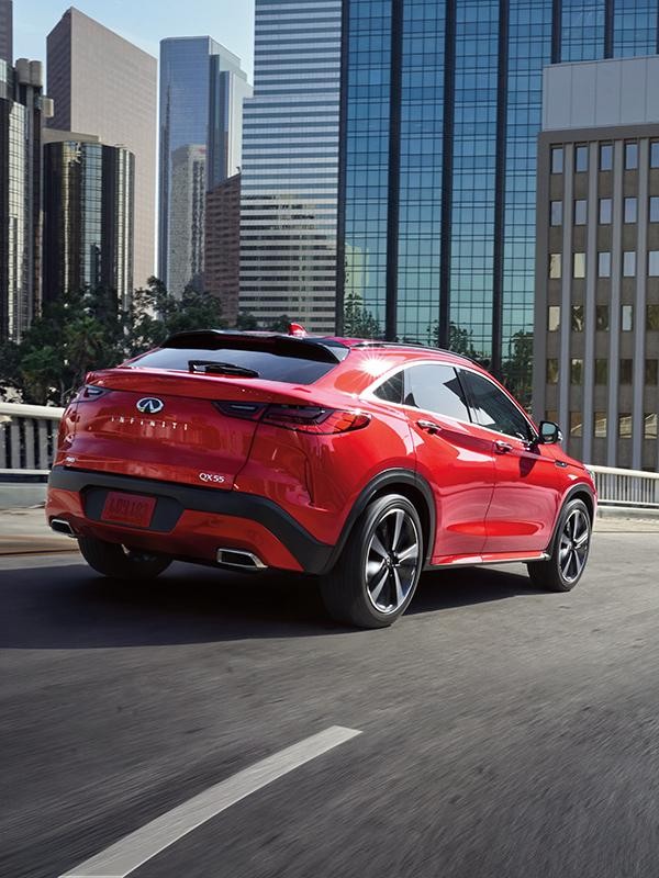 Rear view of a red INFINITI QX55 driving into a city.