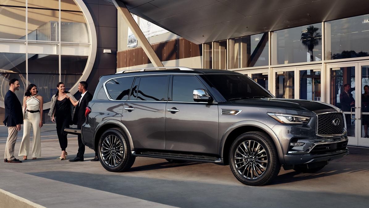 A grey INFINITI QX80 parked in front of a concert hall with people around.