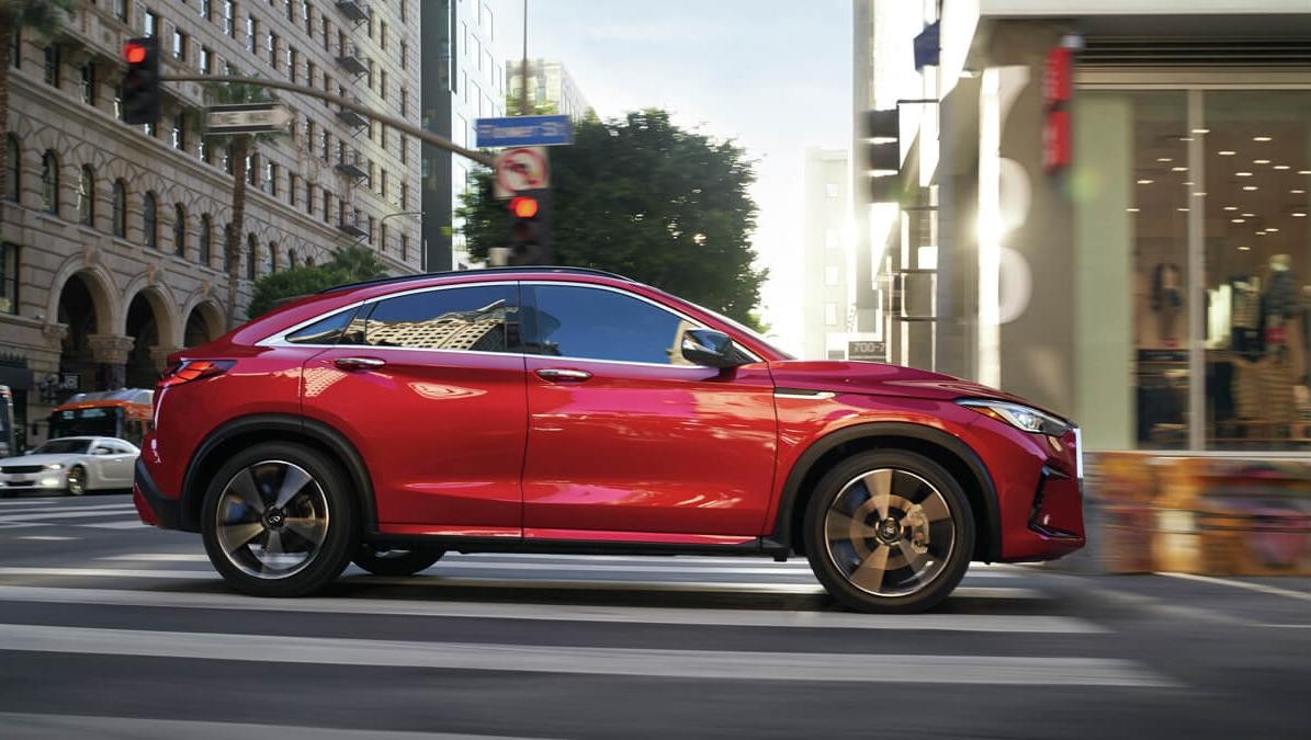 Profile view of a red INFINITI QX55 driving through a city.