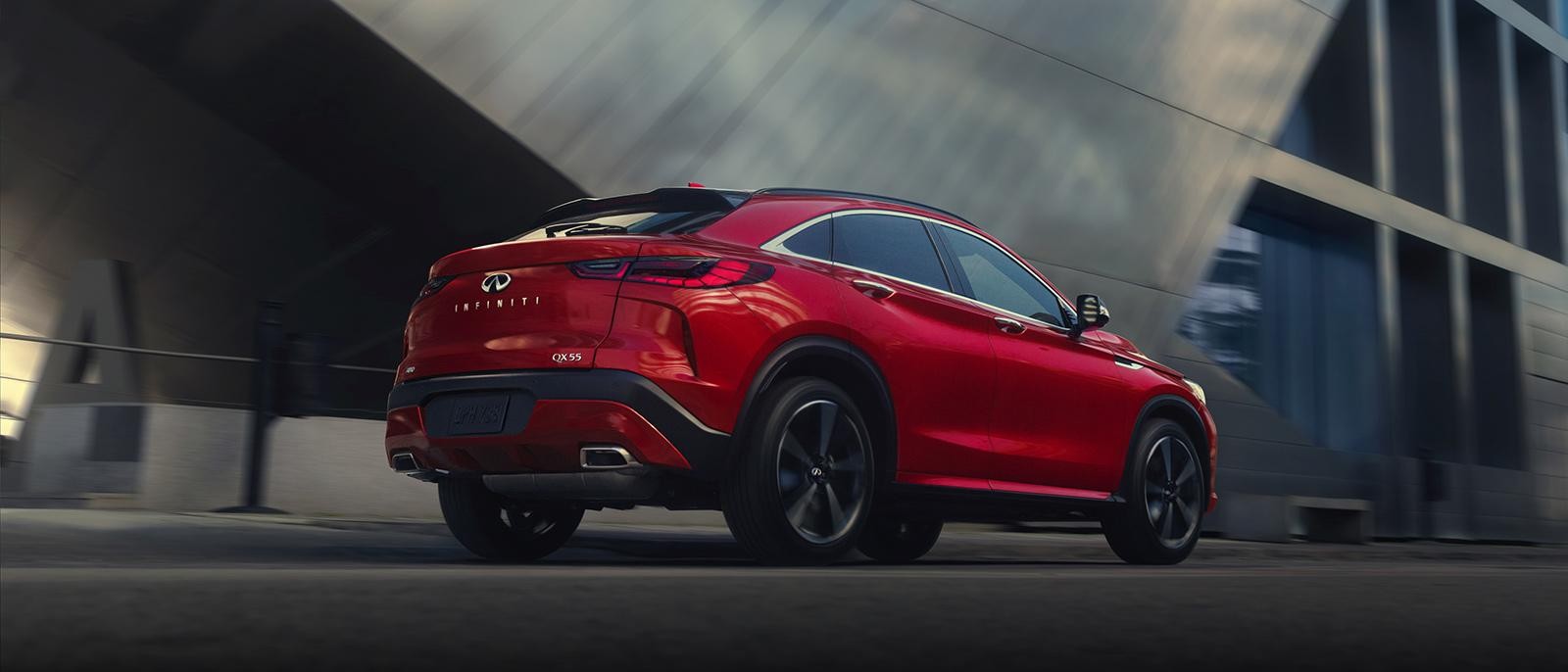 A red INFINITI QX55 driving along a city street.