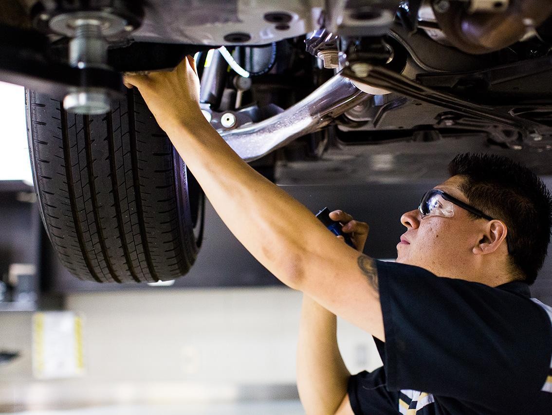 Male service tech examining the wheel and brakes of a Lexus with a flashlight.