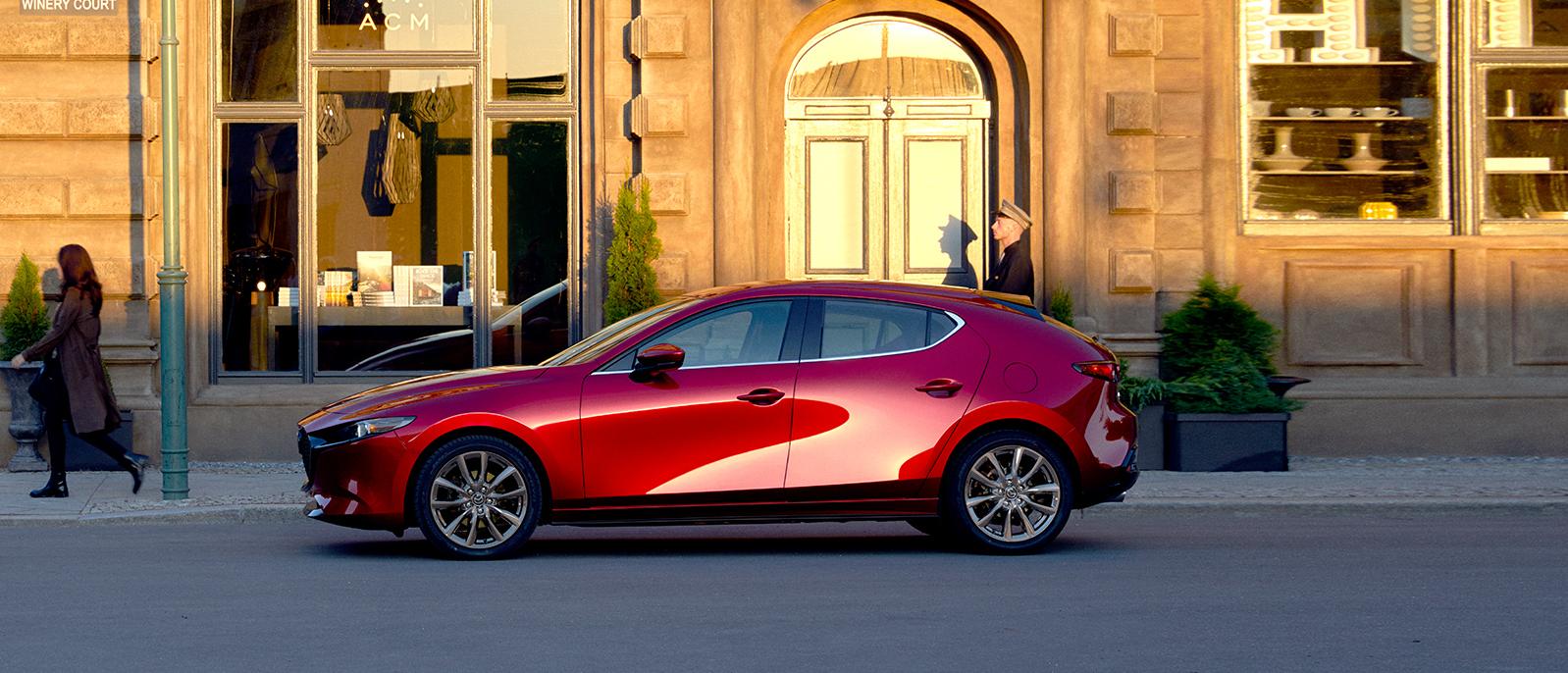 A Red 2020 Mazda3-Hatchback parked in front of an old hotel. A Red 2020 Mazda3-Hatchback parked in front of an old hotel.