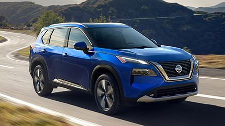 A blue Nissan Rogue driving down a curvy highway.