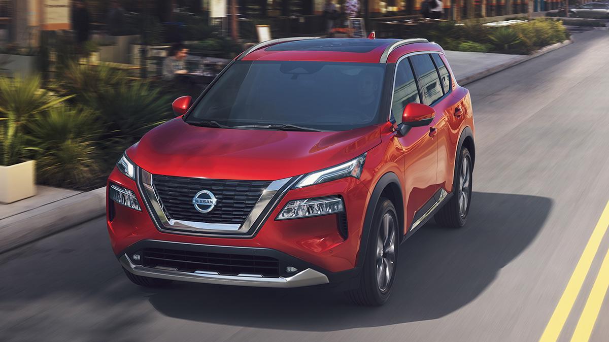 A red Nissan Rogue driving down a city street.