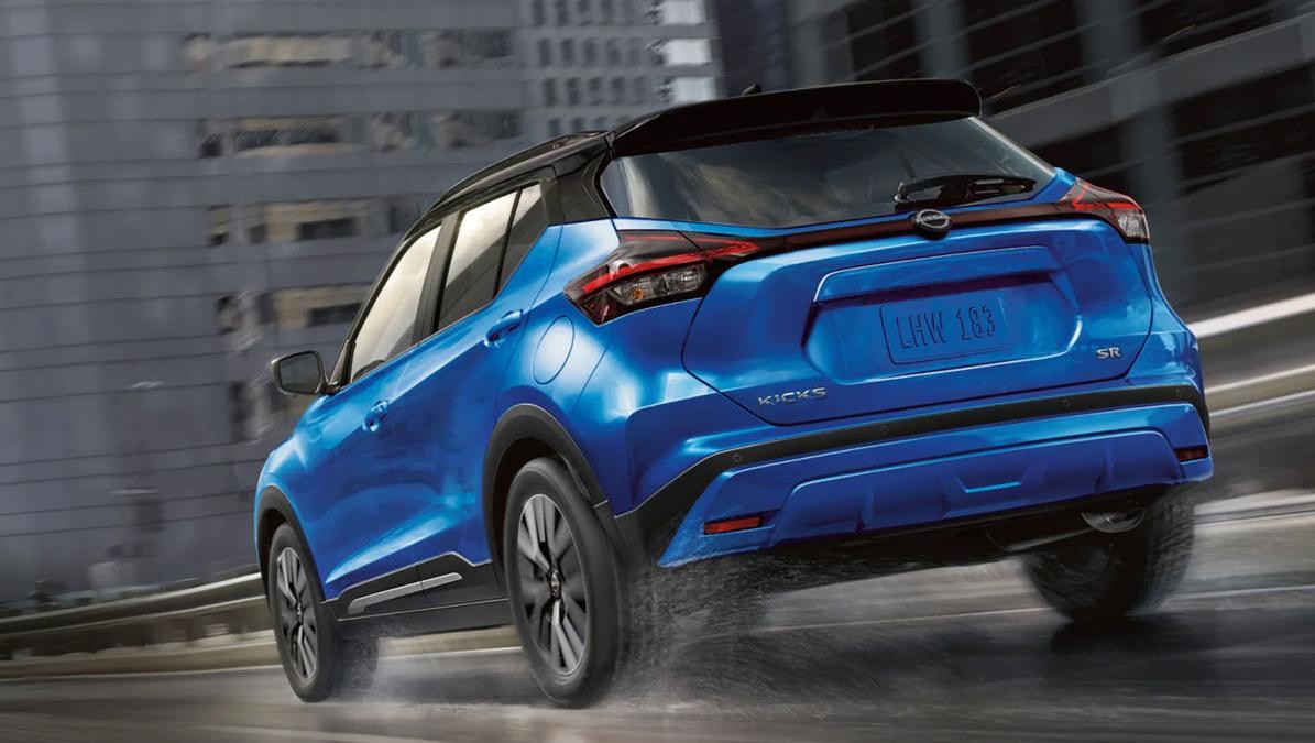 Blue Nissan Kicks driving down a city street in the rain.