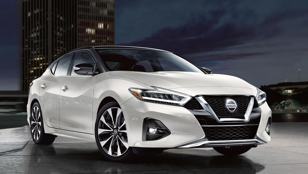 A red 2022 Nissan Maxima parked in front of a cityscape.