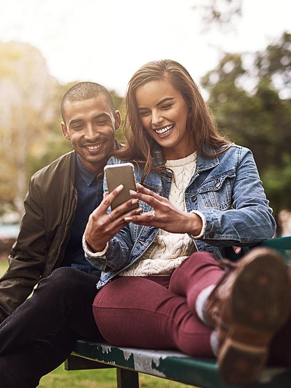 Smiling couple looking at a phone on a park bench Smiling couple looking at a phone on a park bench