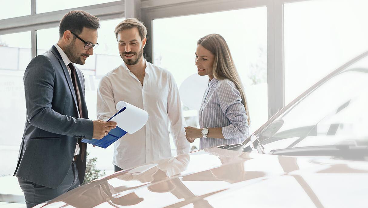 Dealership sales associate helping a smiling couple shop for a new vehicle