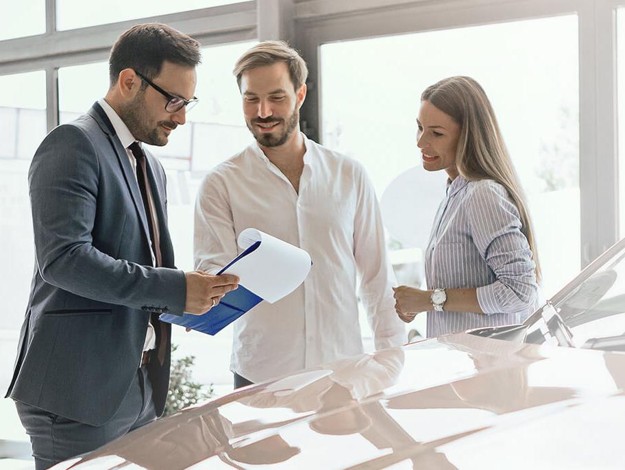 Dealership sales associate helping a smiling couple shop for a new vehicle