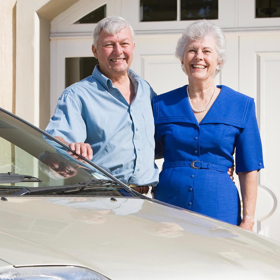 Smiling elderly couple at home, standing by their car