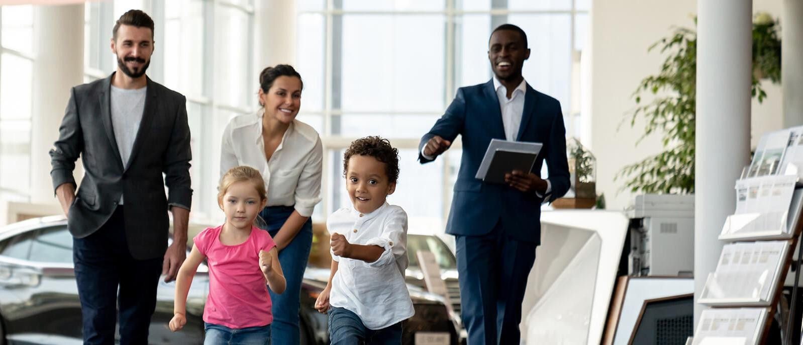 Family with young kids running in a dealership showroom