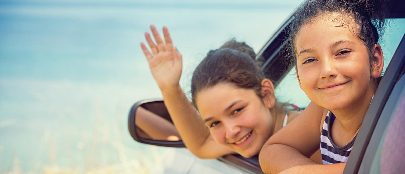 Smiling young girls in a car by the water