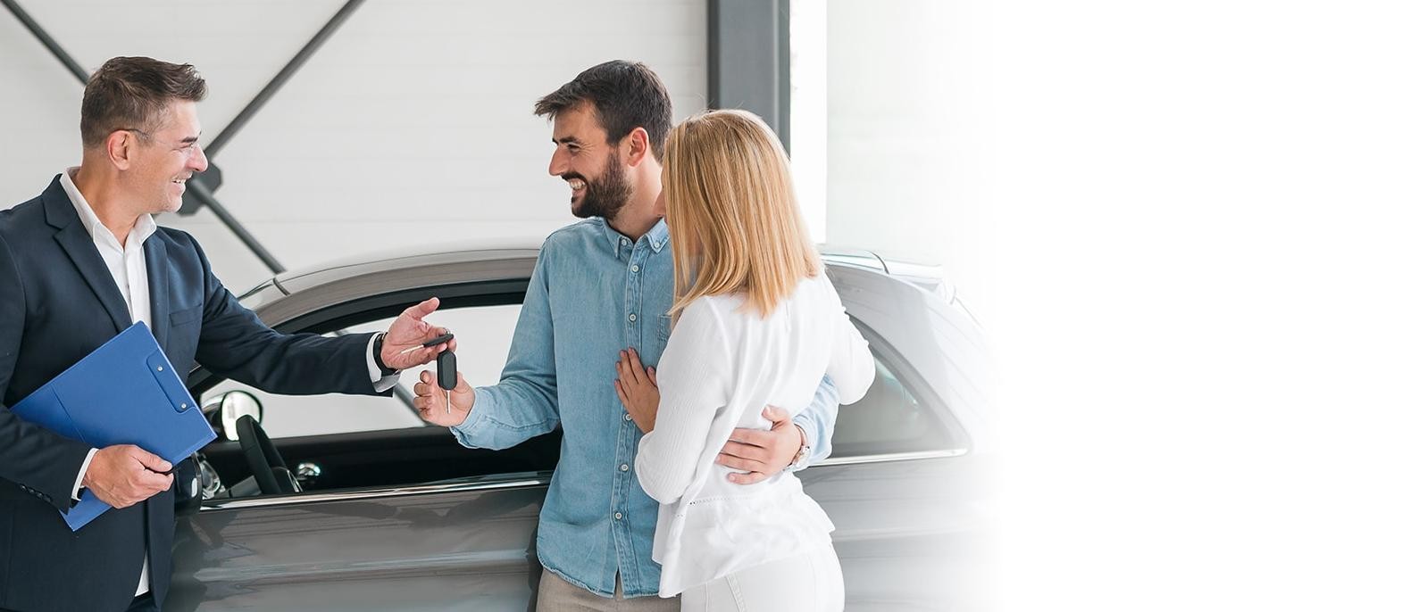 Happy couple with a dealership sales associate looking at a new vehicle