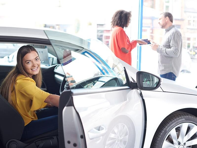 Smiling girl in a car in a dealership vehicle showroom