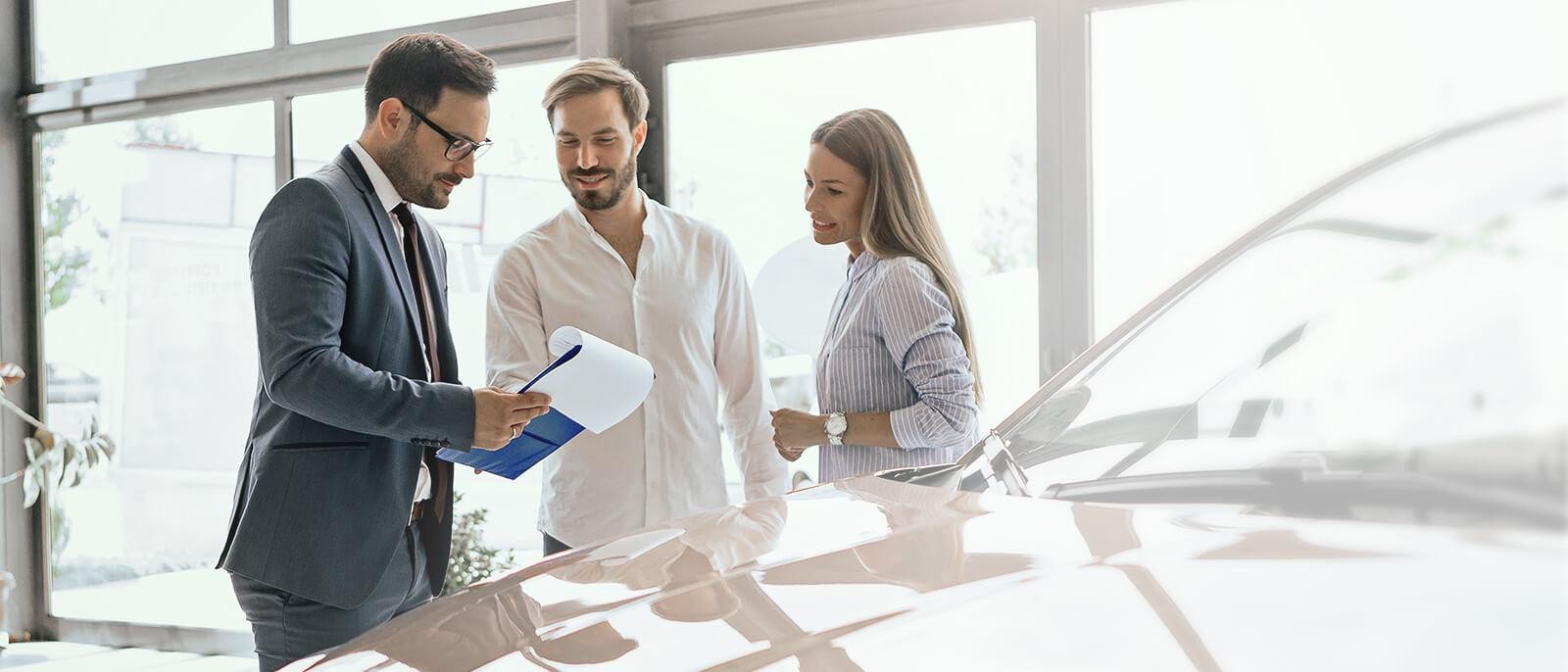 Dealership sales associate helping a smiling couple shop for a new vehicle