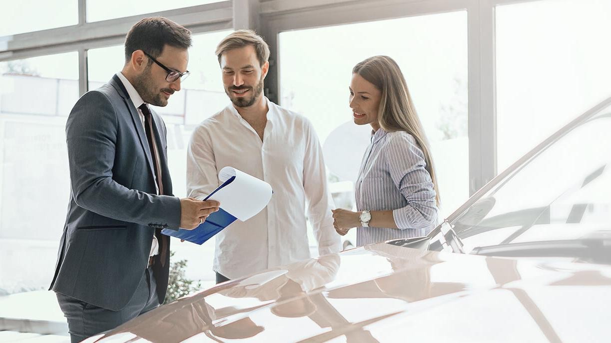 Dealership sales associate helping a smiling couple shop for a new vehicle