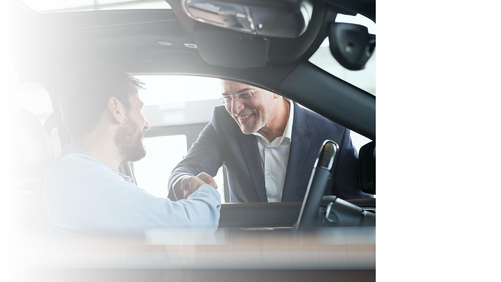 Dealership associate shaking hands with a customer in his new car