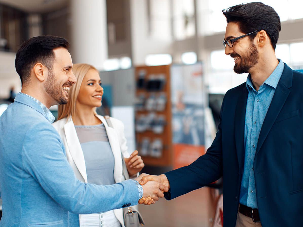 Couple shaking hands with a dealership sales associate