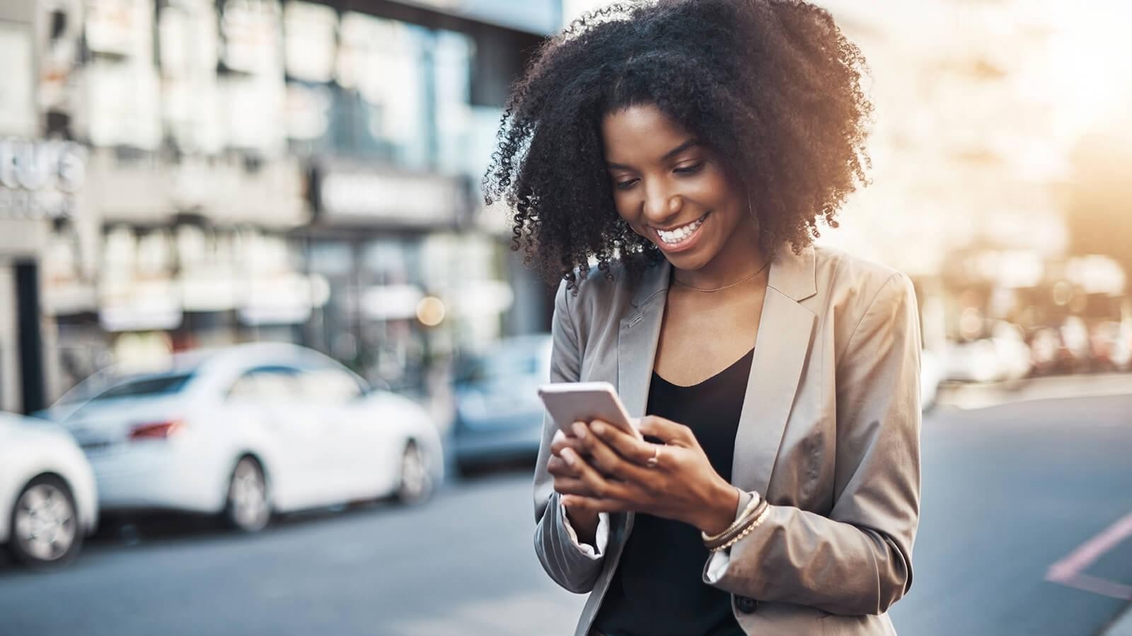 Smiling woman using her cell phone while walking down a street