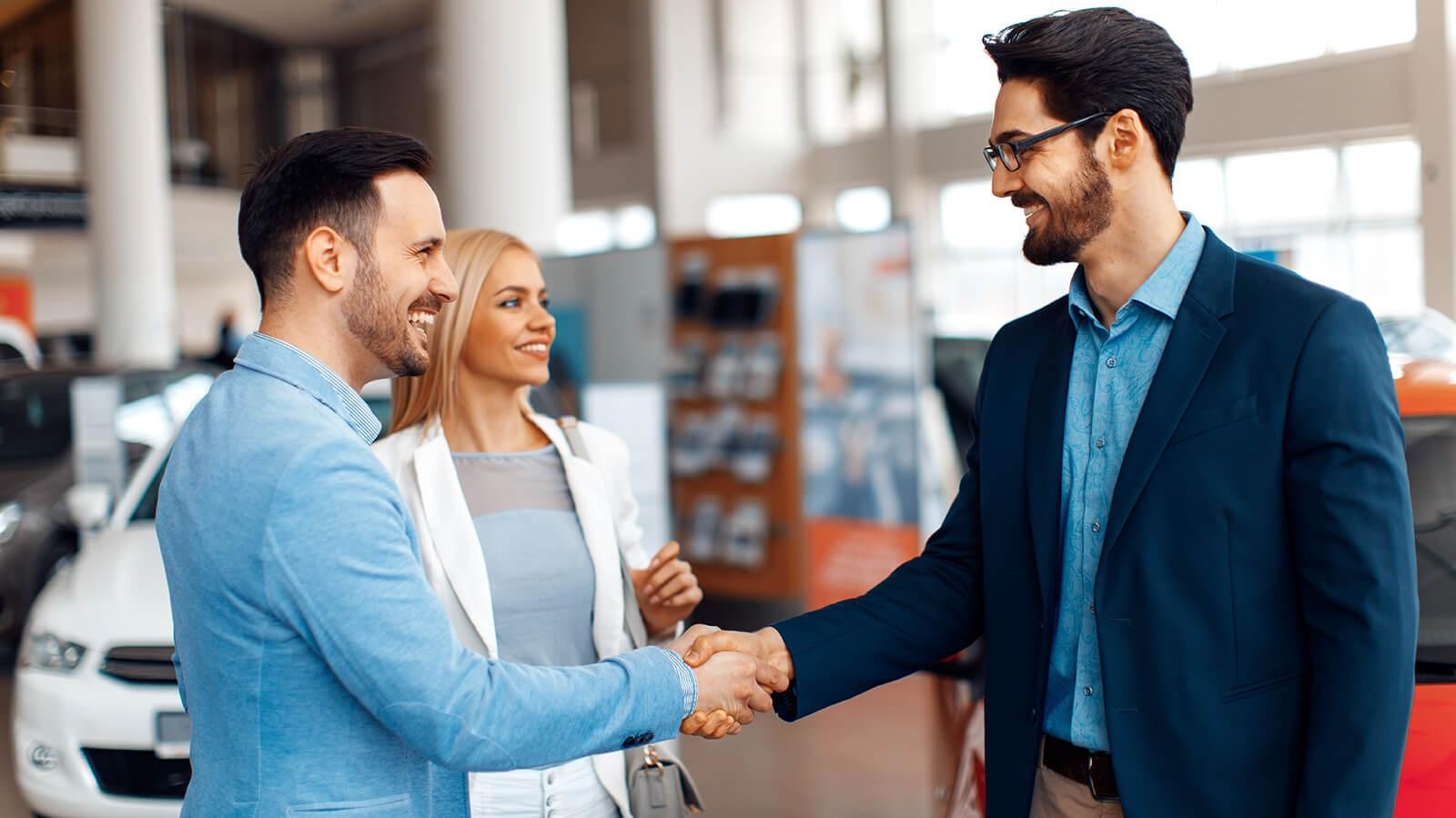 Couple shaking hands with a dealership sales associate