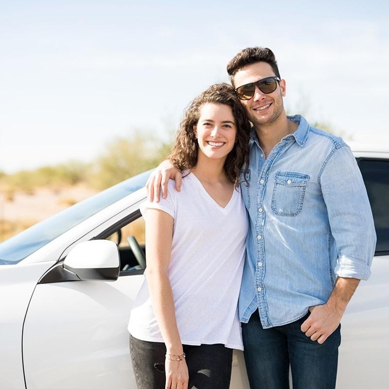 Smiling couple standing in front of their new car