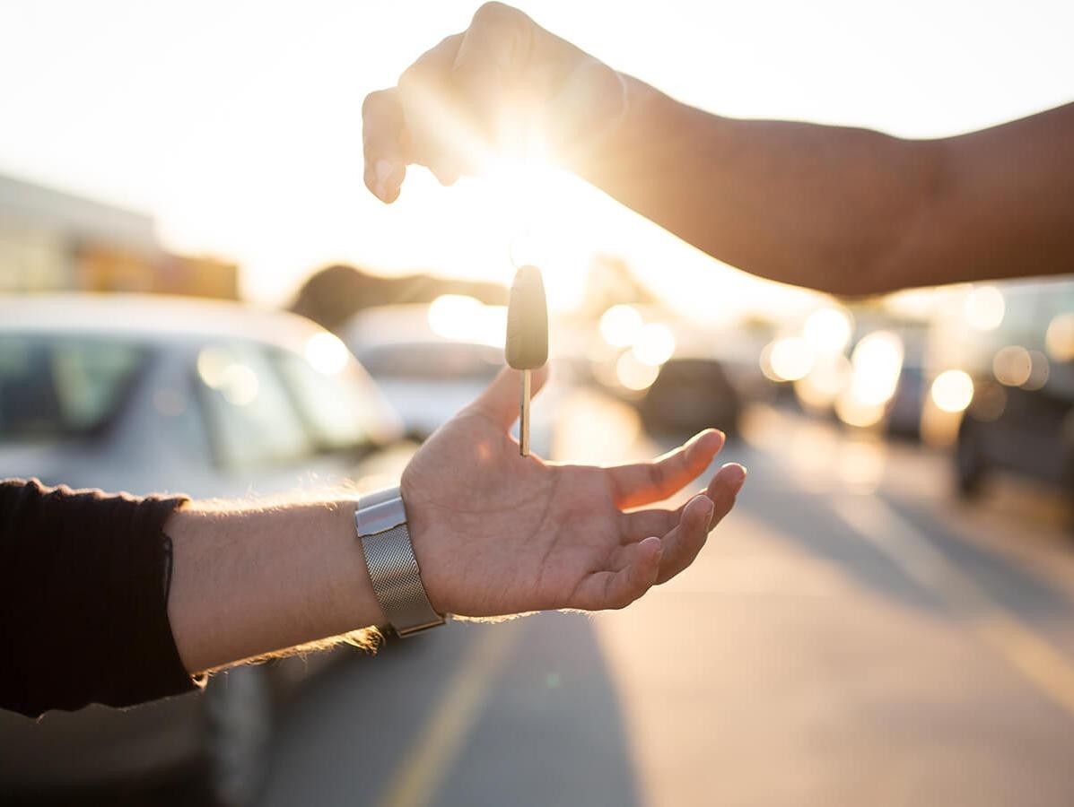 A man's hand giving a car key to another man's hand