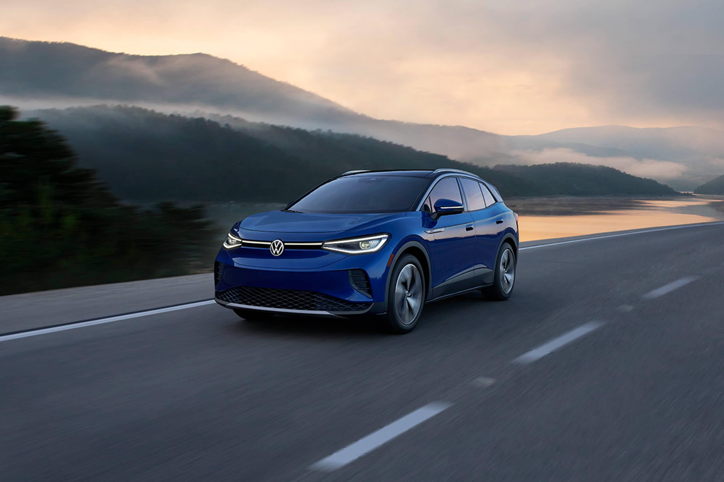An ID.4 in Dusk Blue Metallic drives along a two-lane highway with mountains in the background.