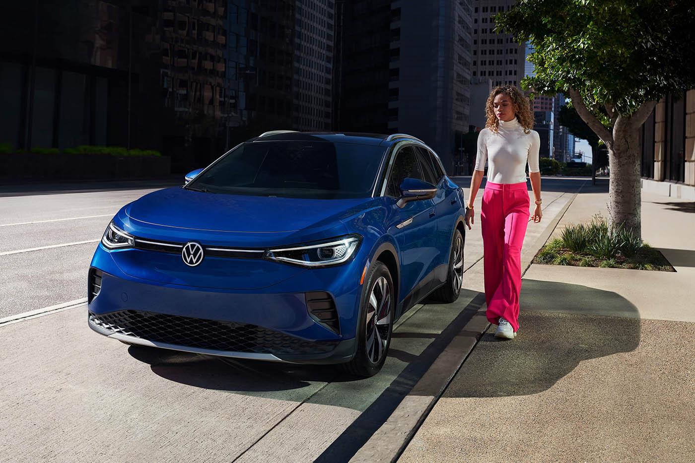 A woman walks towards the driver’s side of an ID.4 in Dusk Blue Metallic, shown parked on an urban street.