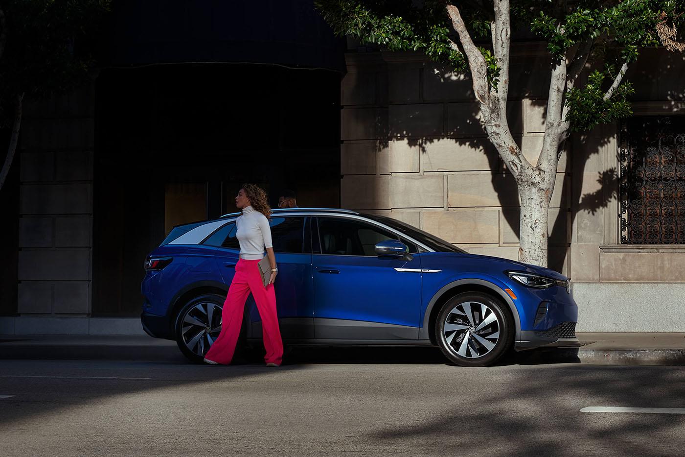 A woman walks away from the passenger side of an ID.4 in Dusk Blue Metallic, parked on an urban street.