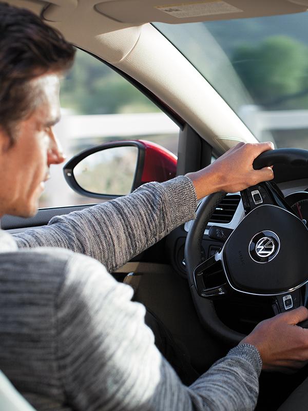 Interior view of a man driving a new Volkswagen along a country road.