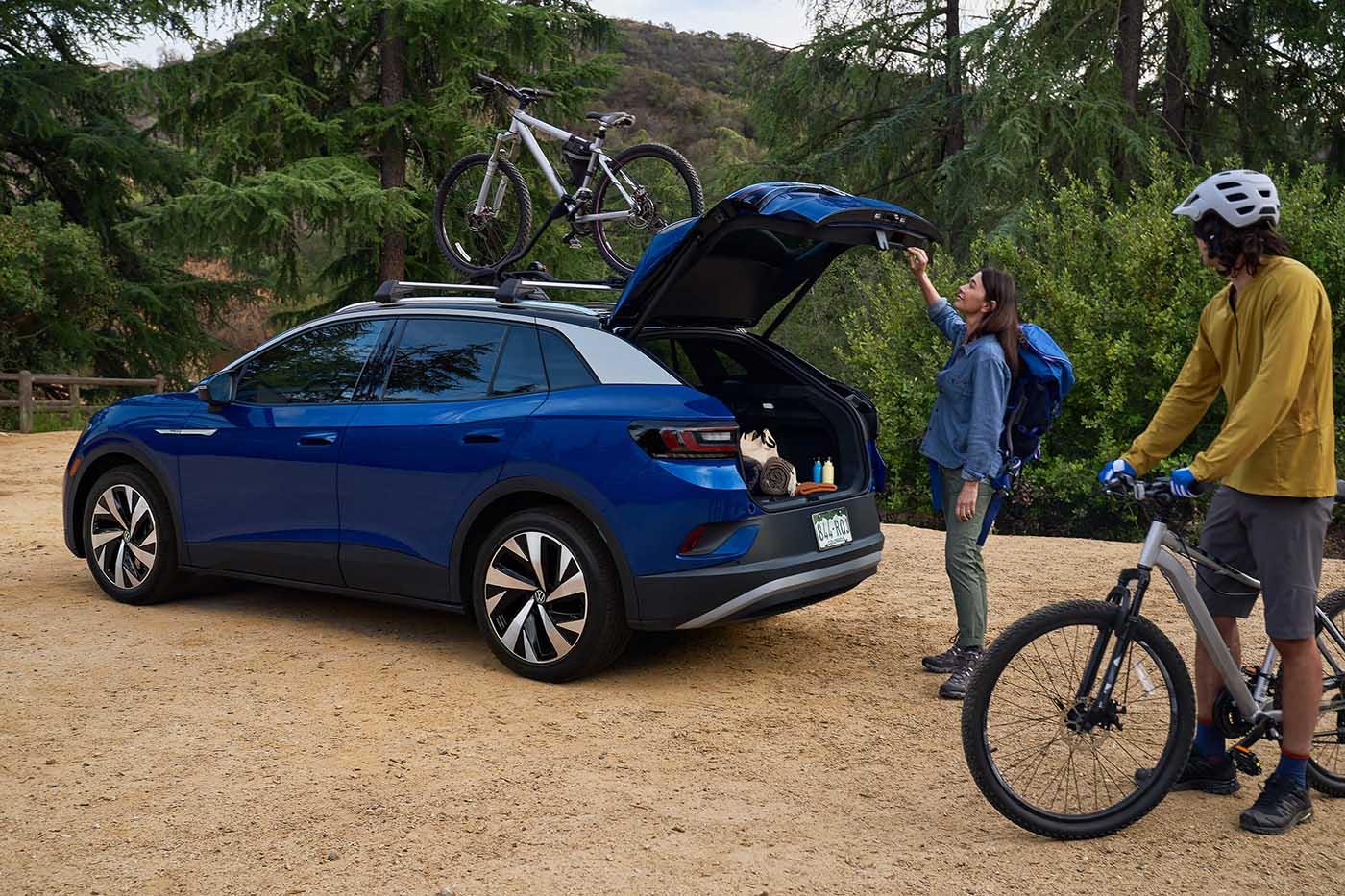 A man and woman load mountain bicycles onto an ID.4 in Dusk Blue Metallic with cross bars and a bike attachment that’s parked in a natural, outdoor setting.