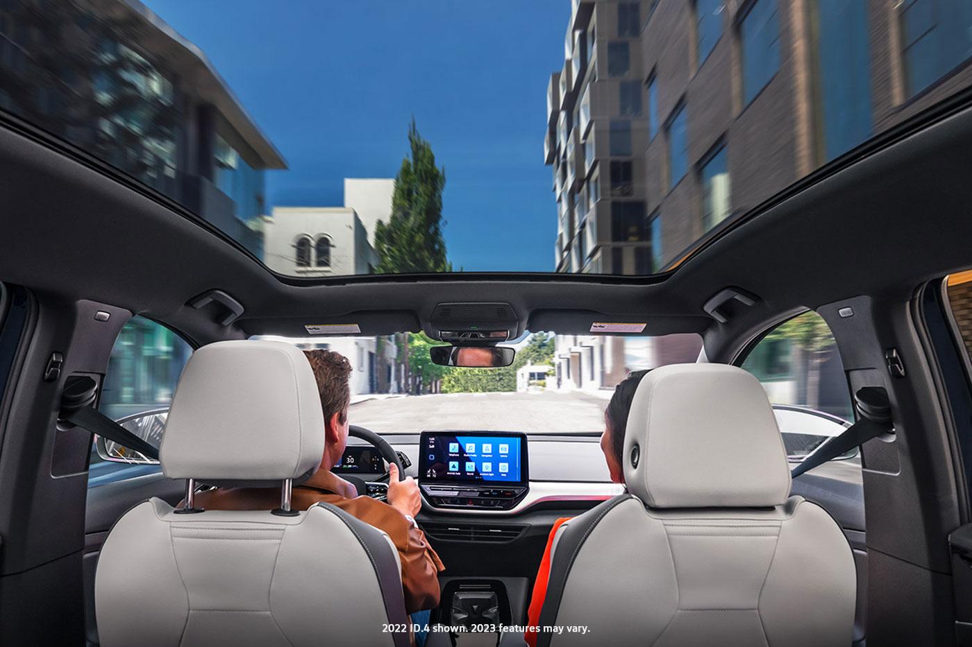 A forward shot of a man and woman driving an ID.4 with the sunshade open as they head down an urban street.