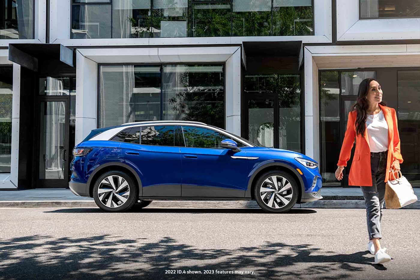 A woman walks away from an ID.4 in Dusk Blue Metallic that’s parked on an urban street.