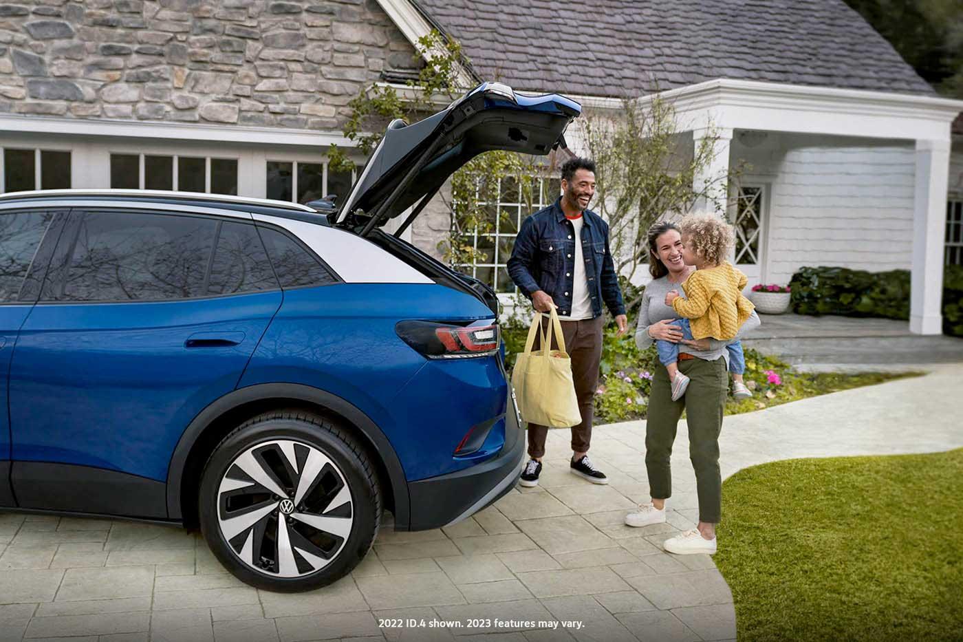 A young family loads a bag into the cargo area of an ID.4, shown in Dusk Blue Metallic parked in a residential home’s driveway.