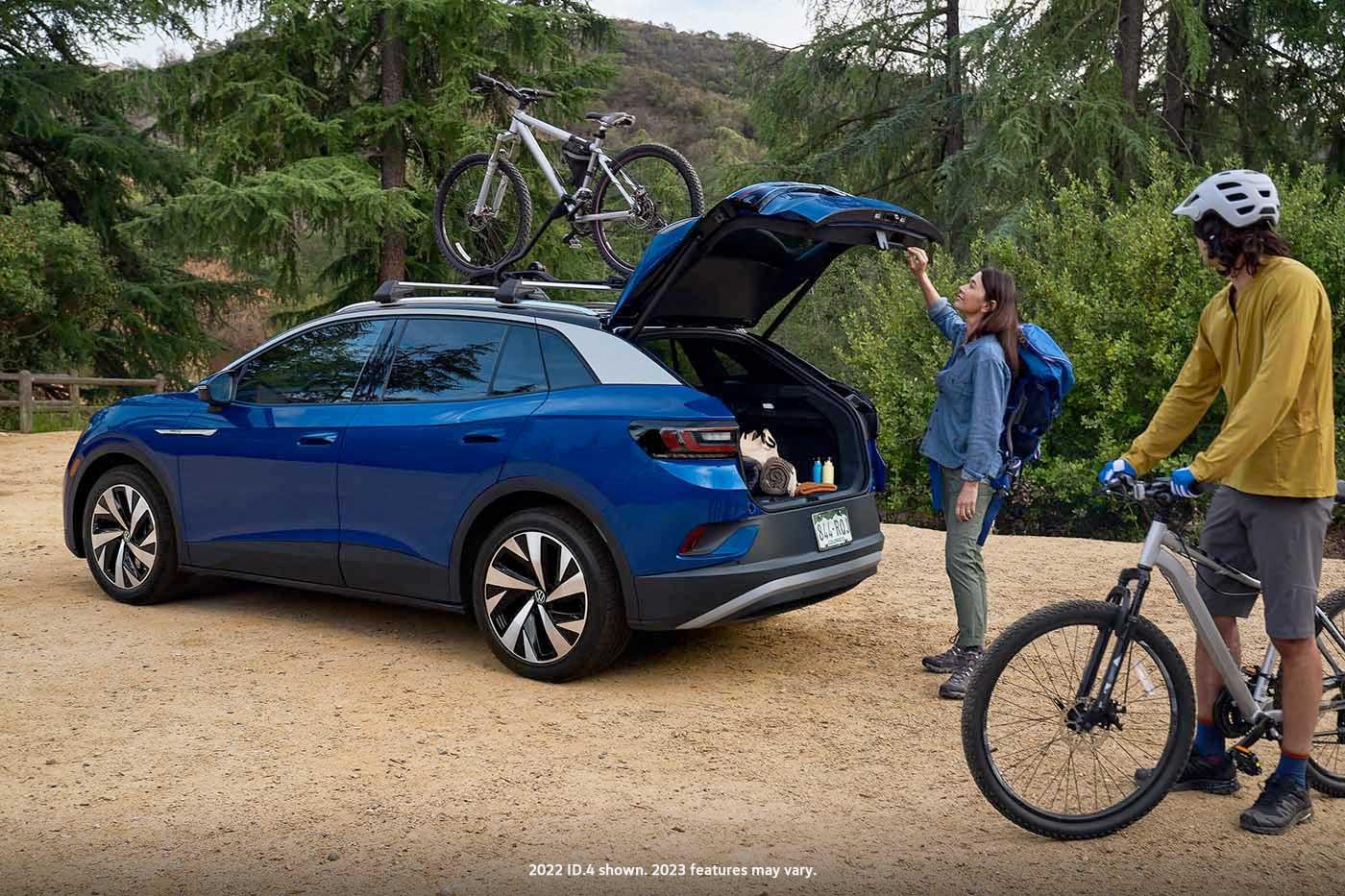 A man and woman load mountain bicycles onto an ID.4 in Dusk Blue Metallic with cross bars and a bike attachment that’s parked in a natural, outdoor setting.
