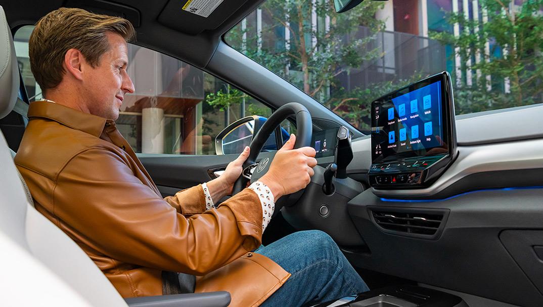 An interior view of a man driving an ID.4, with on hand on the steering wheel, and his focus on the center console display.