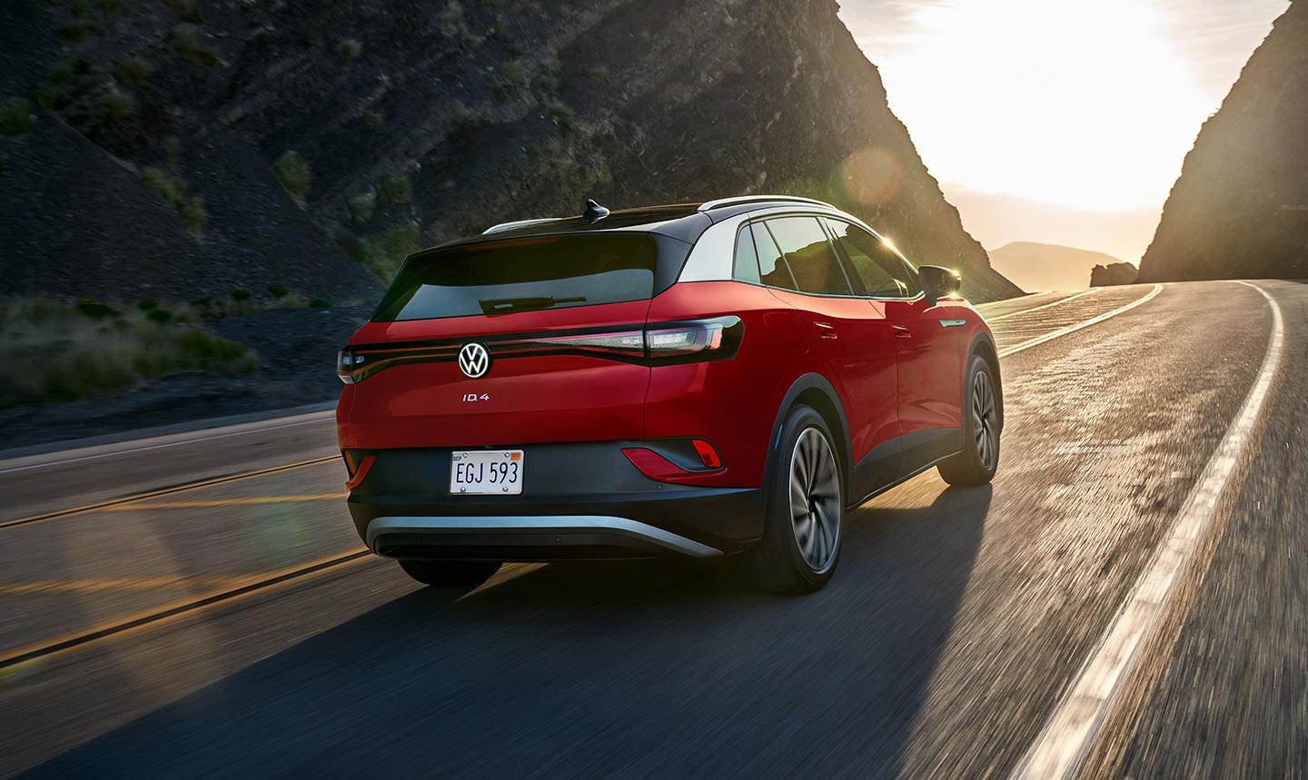 A rear view shot of an ID.4 Pro S Plus in Aurora Red Metallic driving up a two-lane mountain road with the sun shining in the distance.