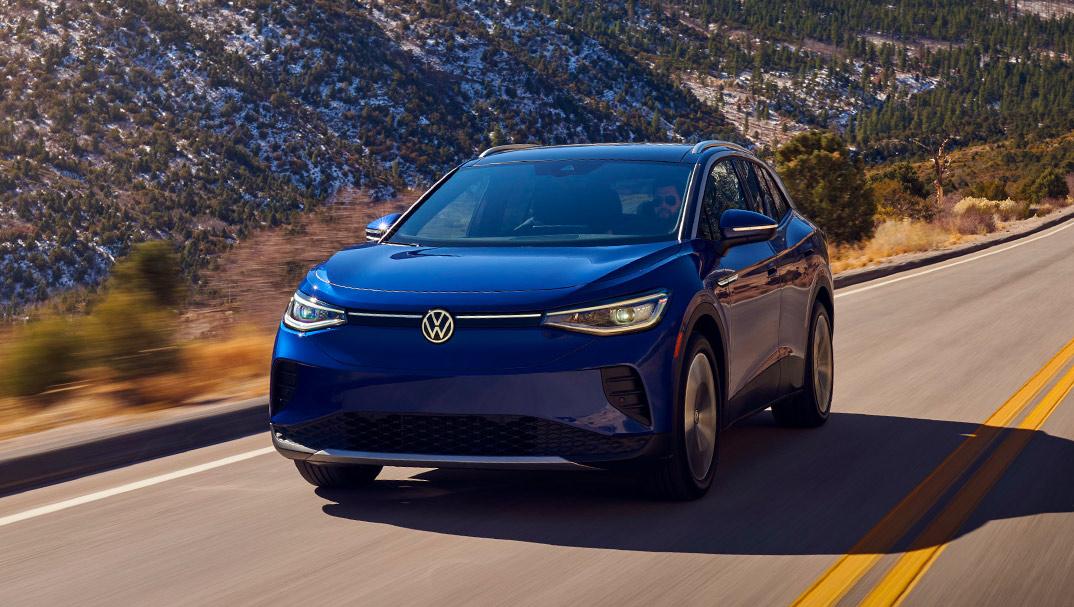 An ID.4 in Dusk Blue Metallic drives along a two-lane highway with mountains in the background.