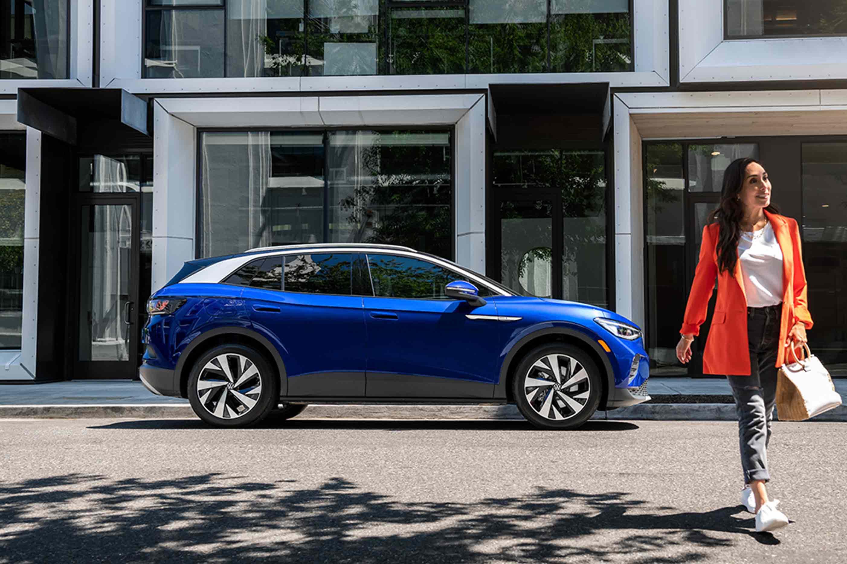 A woman walks away from an ID.4 in Dusk Blue Metallic that’s parked on an urban street.