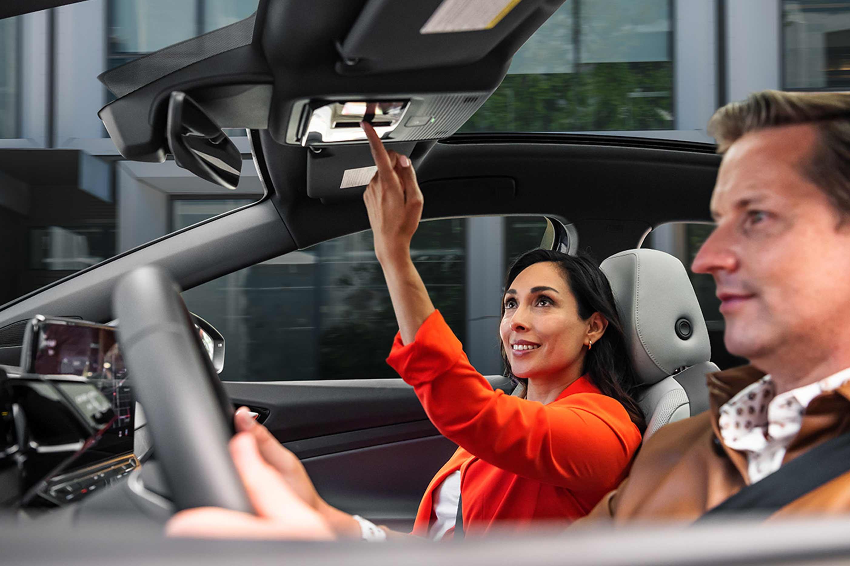 A man and woman sit in the front seats of an ID.4 while the woman in the passenger seat adjusts the controls for the sunshade.