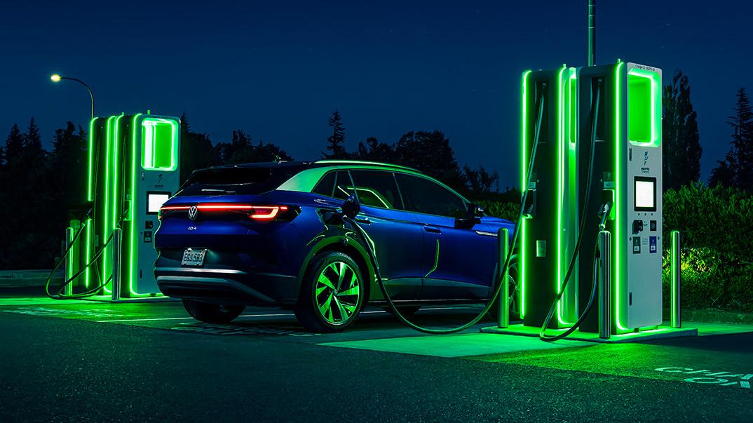 An ID.4 in Dusk Metallic Blue as it is parked at night next to a neon lit charging station.