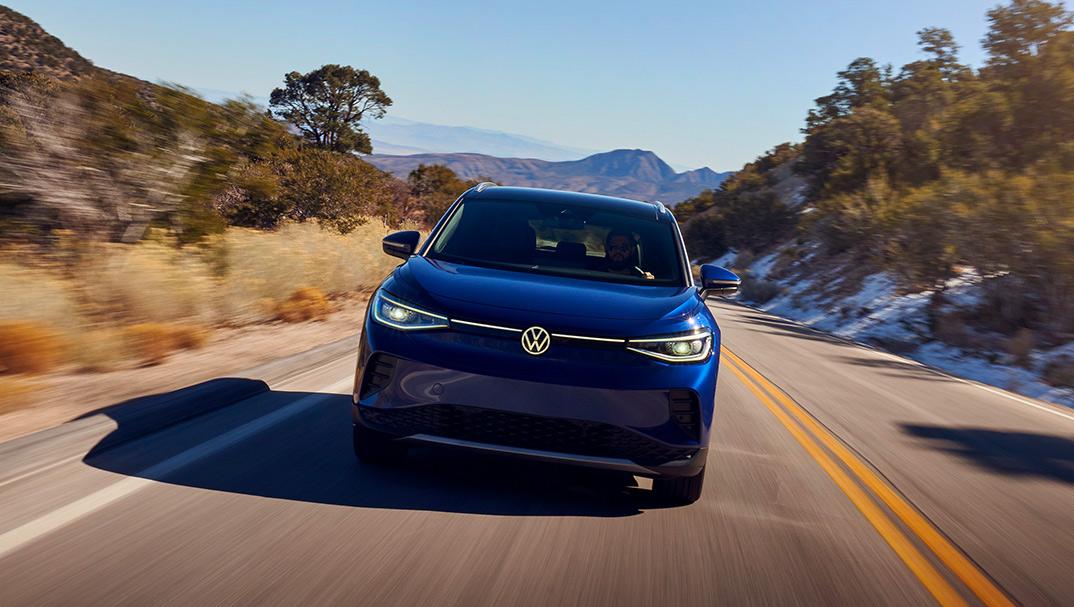 A front shot of an ID.4 in Dusk Blue Metallic cruising down a 2-lane highway in a natural setting.