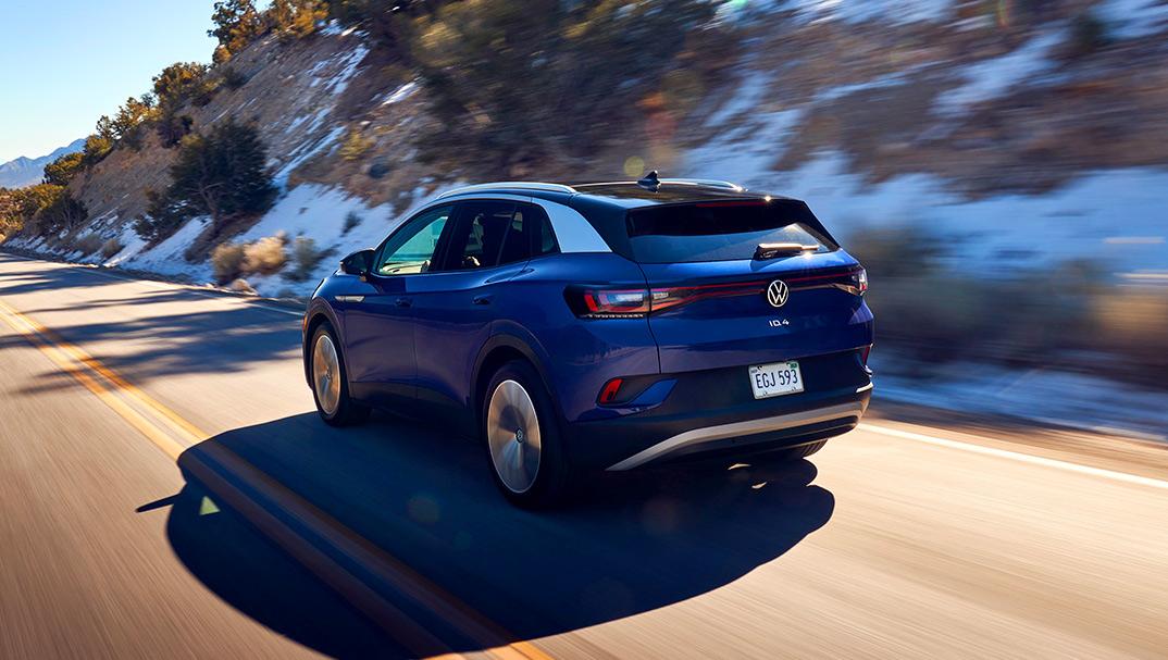 A ¾ rear shot of an ID.4 in Dusk Blue Metallic speeds up a two-lane highway in a mountain setting.
