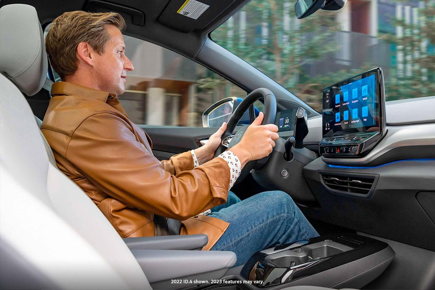 An interior view of a man driving an ID.4, with on hand on the steering wheel, and his focus on the center console display.