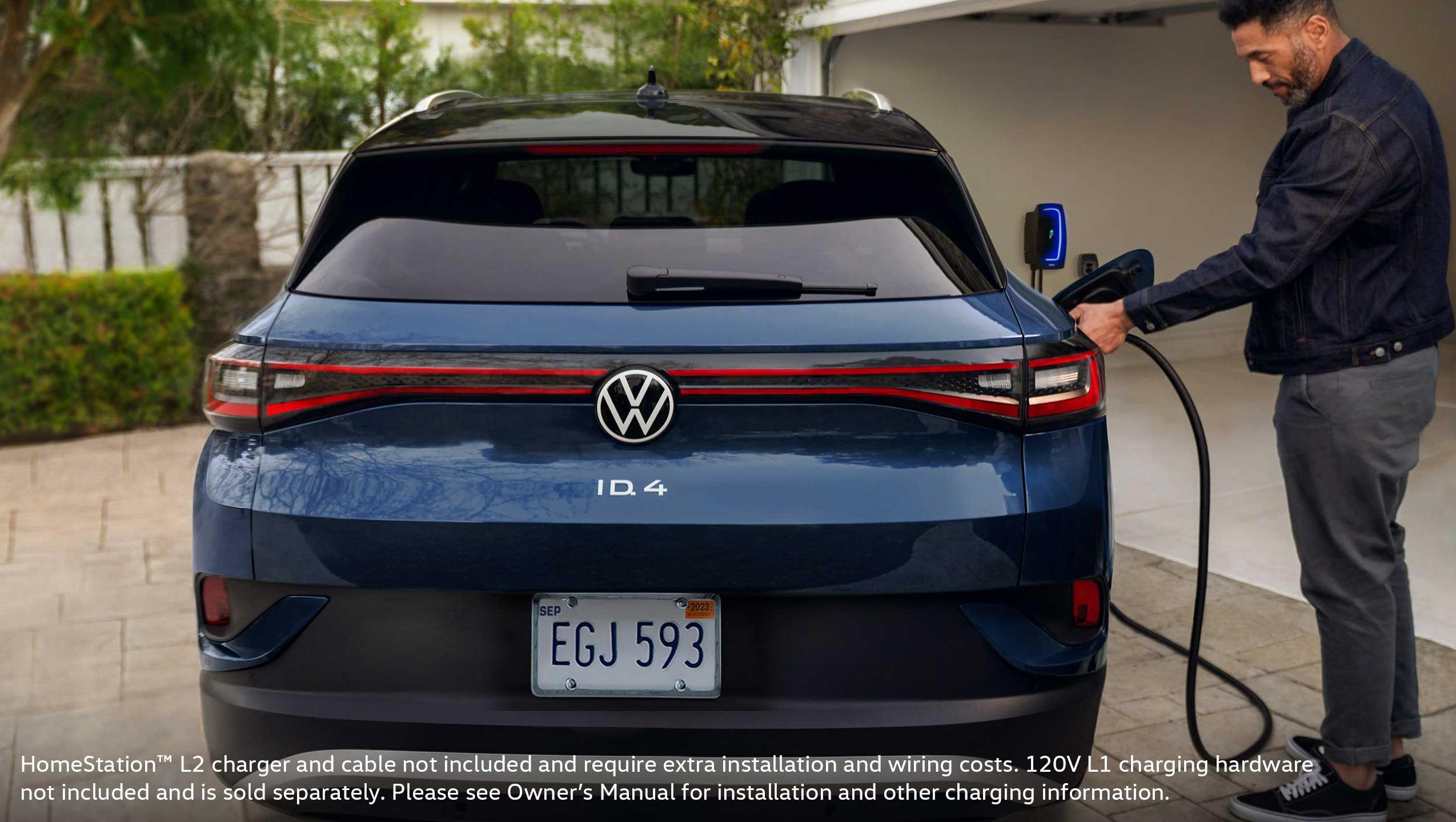 A rear view shot of the ID.4 SUV and a man plugging in a charging cable into the vehicle outside his home garage.
